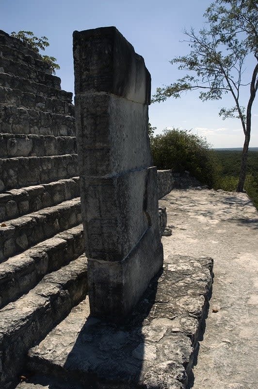Stone steps with a tall rectangular pillar on a rocky platform beside a tree