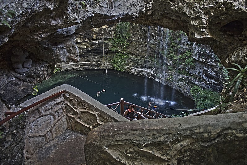 Stone stairway descending into Cenote Saamal beneath small waterfalls