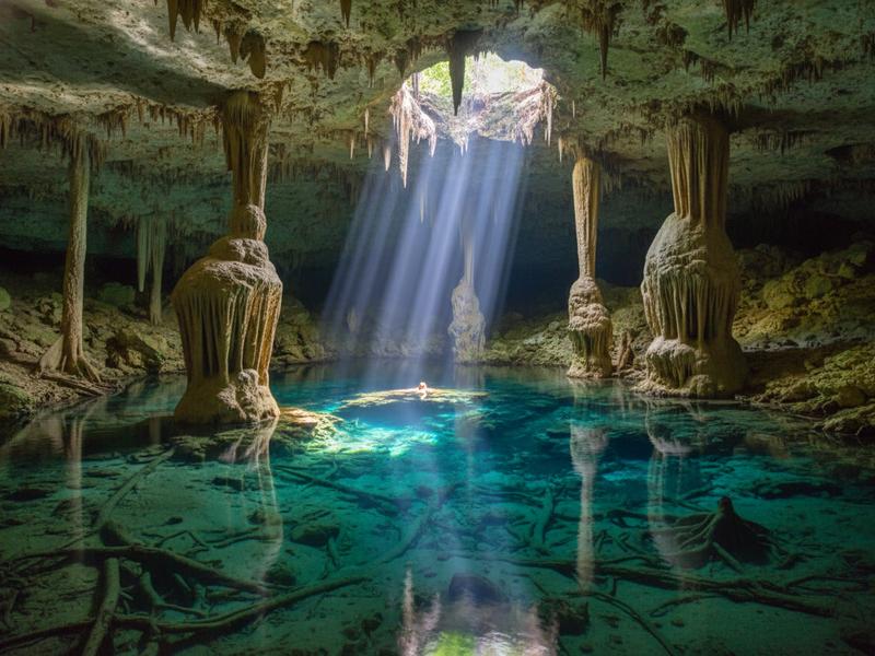 Swimmer floating in Gran Cenote Tulum Mexico with stalactites and crystal clear turquoise water