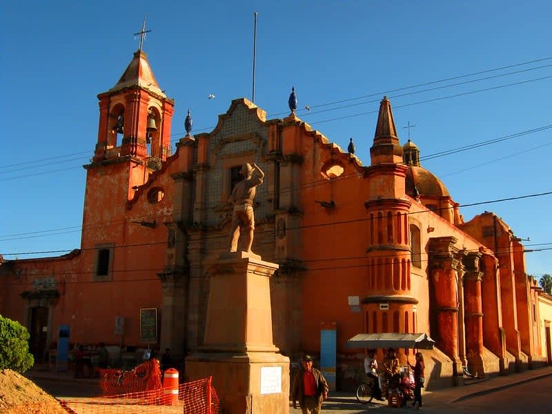 Orange church on a street corner with a bell tower, decorative facade, overhead wires, and a statue in front