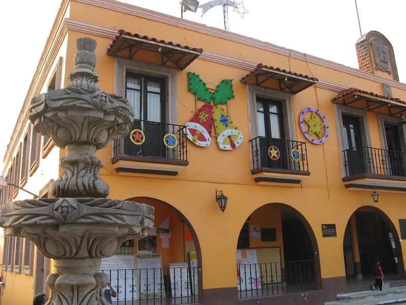 Yellow civic building with arches, balconies, festive decorations, and a carved stone fountain in front