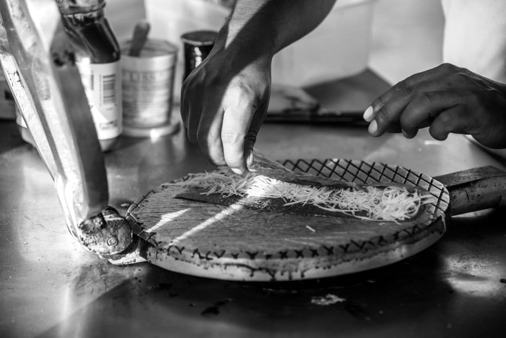 Hands grating Edam cheese over a hot marquesita press