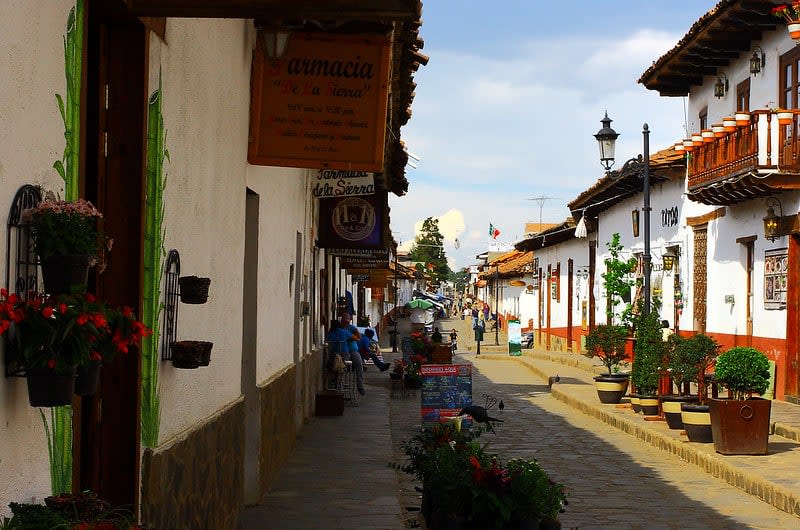 Cobblestone street lined with whitewashed buildings, balconies, and potted plants in Mazamitla