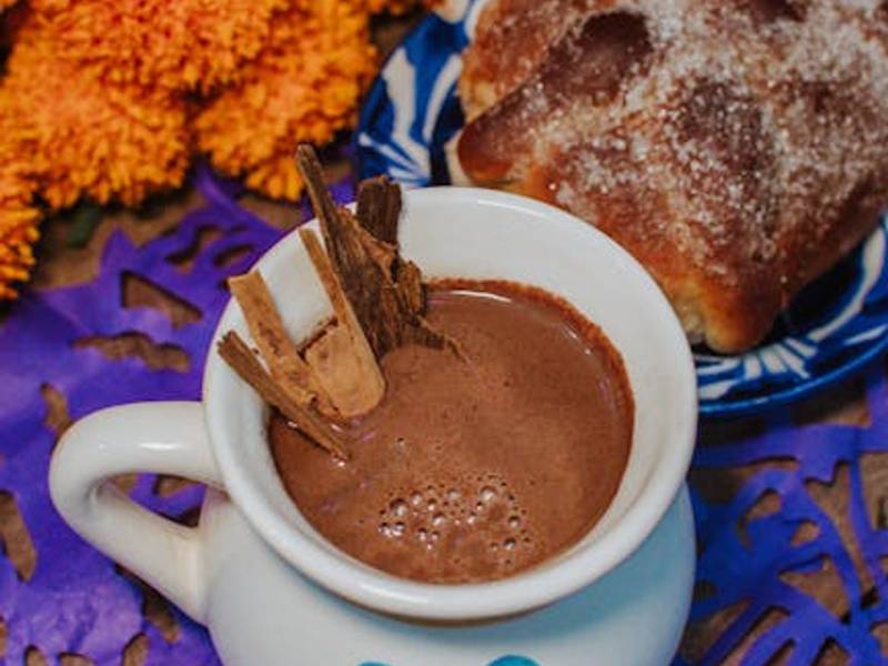 Mexican hot chocolate in a clay mug with cinnamon sticks and chocolate tablets