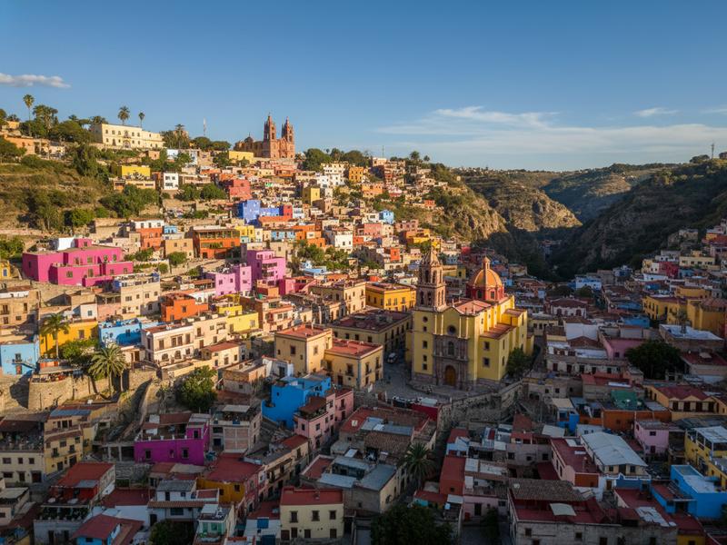 Guanajuato's colorful hillside houses in shades of yellow, pink, orange, and blue cascading down a narrow canyon with colonial spires