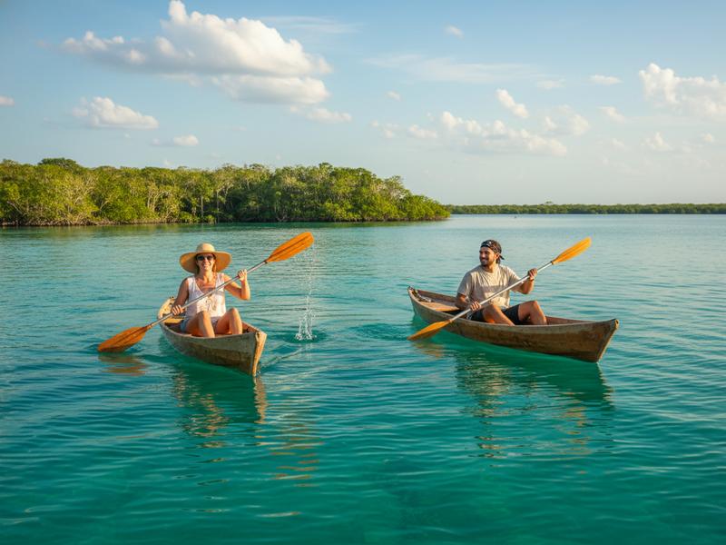Kayaker paddling across the turquoise waters of Bacalar Lagoon Mexico with multiple shades of blue visible