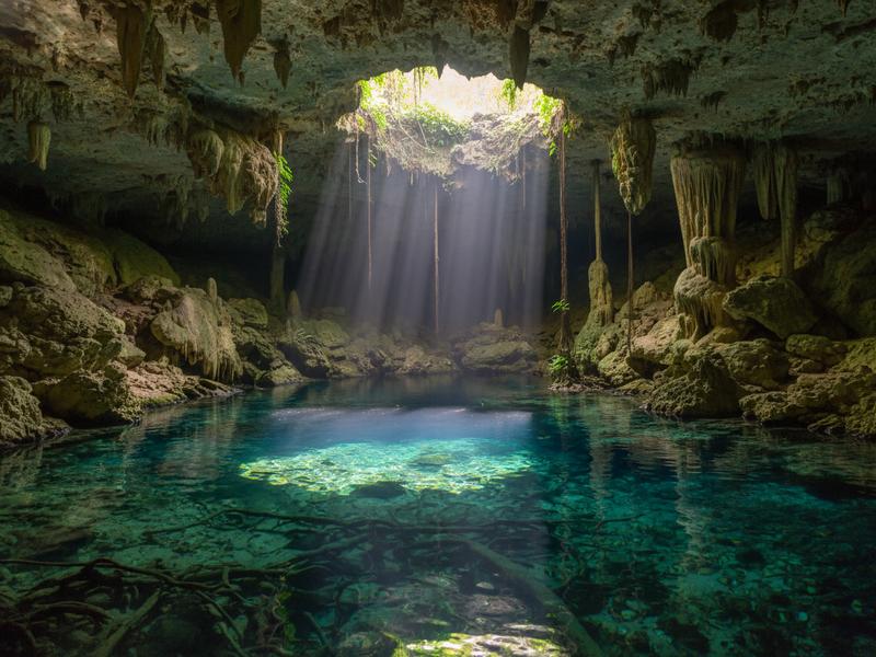 Crystal clear cenote in the Yucatan Peninsula with swimmers enjoying the natural sinkhole surrounded by jungle