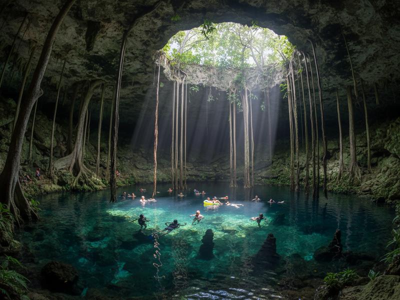 Travelers swimming in a natural cenote in Yucatán Mexico with crystal clear turquoise water and limestone formations