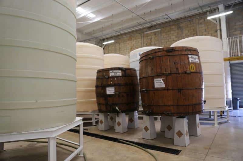 Large white tanks and wooden barrels inside a distillery room
